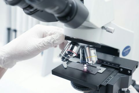 Gloved hand turning the objective lenses of a laboratory microscope